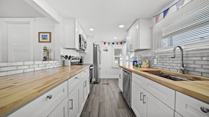 A modern kitchen with white cabinets, wooden countertops, a stainless steel refrigerator, and a window with blinds. - Beachfront · Heated Pool & Spa · Balcony Views (Bradenton Beach)