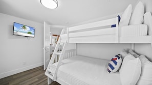 A bunk bed room with a television on the wall, a door leading to another room, and a wooden floor. - Beachfront · Heated Pool & Spa · Balcony Views (Bradenton Beach)