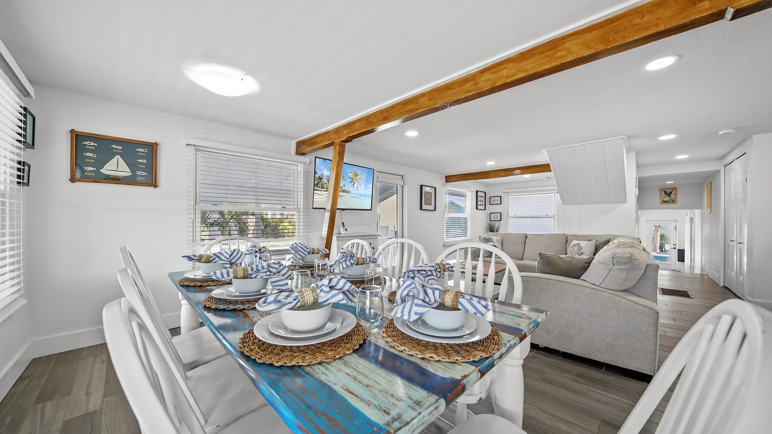 A dining area with a wooden table set for four, white chairs, and a television mounted on the wall.