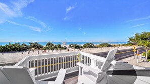 A beachfront view with a white railing, a clear sky, and a road with a pedestrian crossing. - Beachfront · Heated Pool & Spa · Balcony Views (Bradenton Beach)