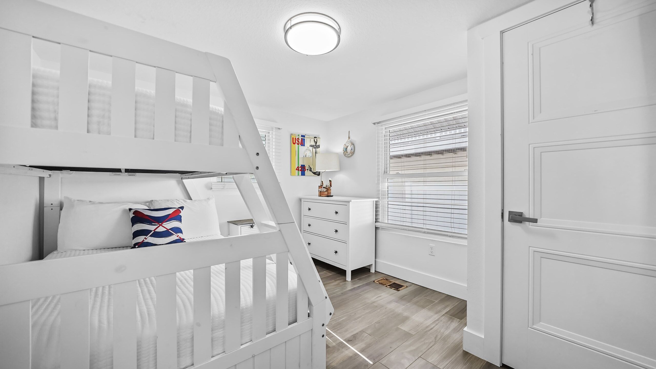 A room with bunk beds, a dresser, a door, and a window with blinds.