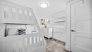 Une chambre avec des lits superposés, une commode, une porte et une fenêtre avec des stores.