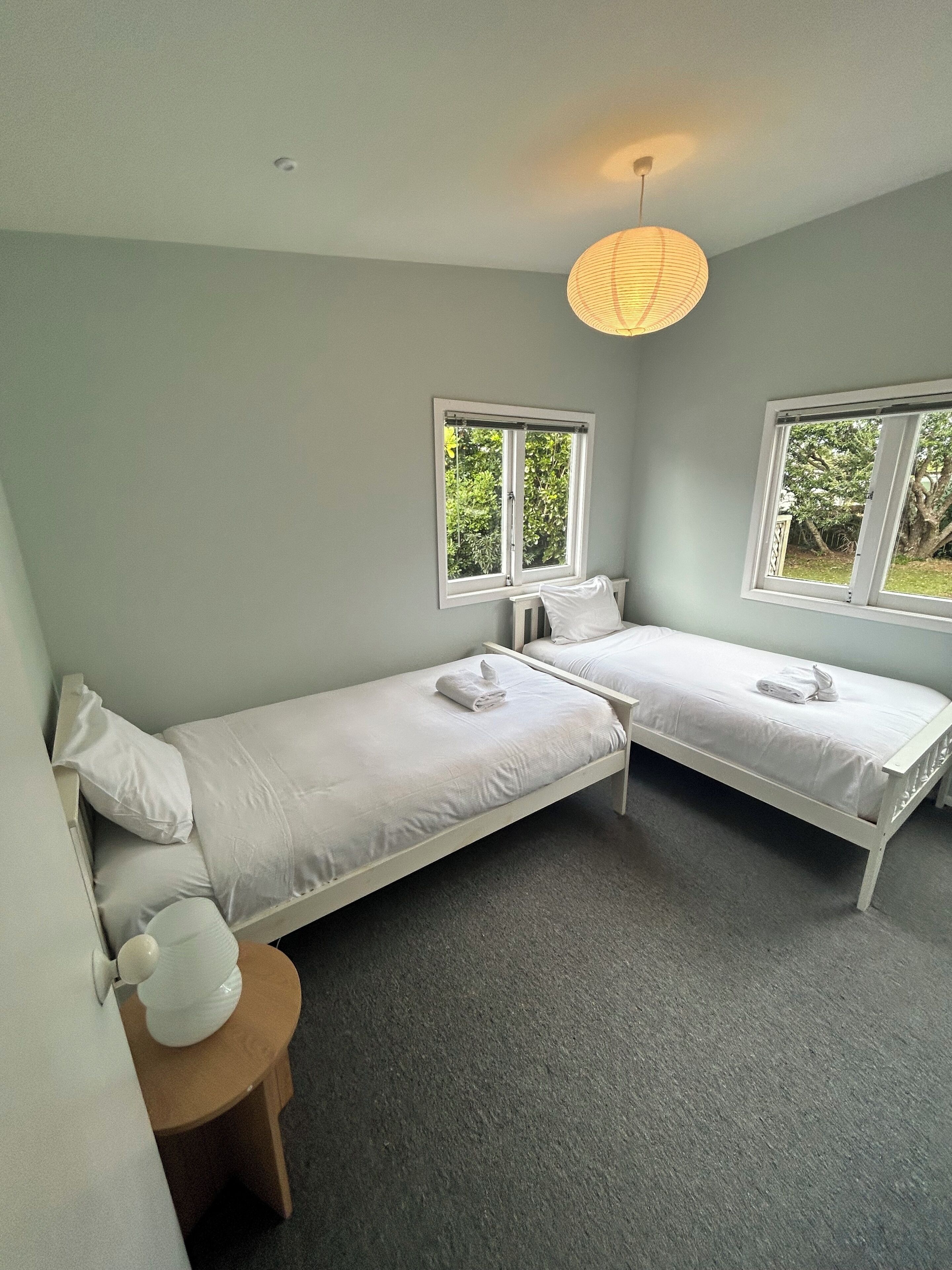 A room with two single beds, a small round table, and a window with a view of greenery.