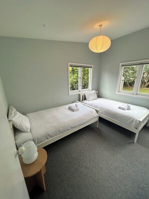 A room with two single beds, a small round table, and a window with a view of greenery. - Oneroa Holiday House (Waiheke Island)