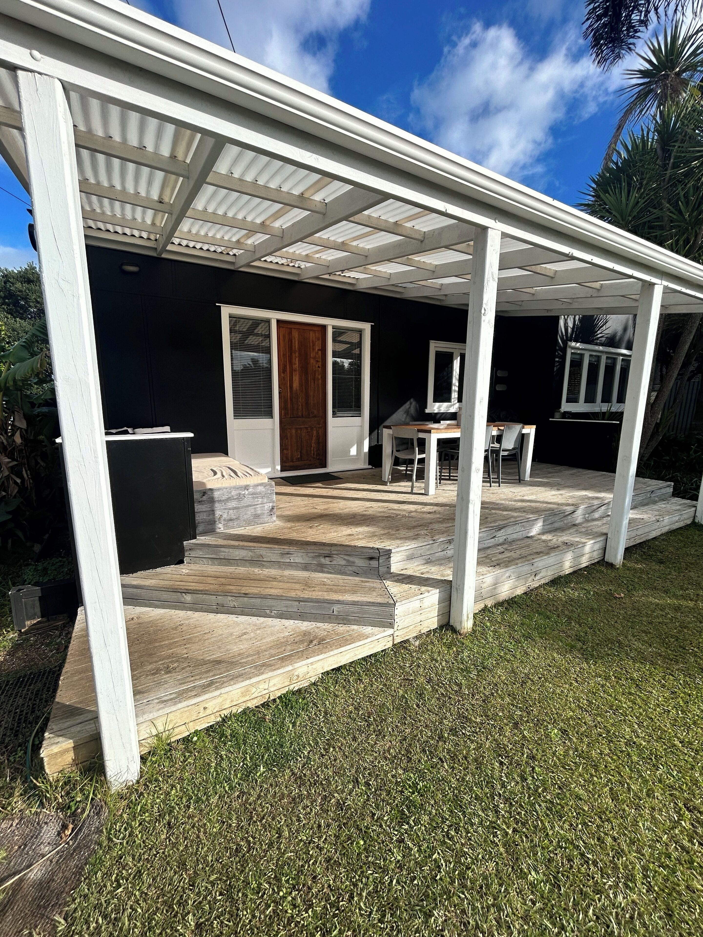 A covered outdoor area with a wooden deck, a door, and a table with chairs.