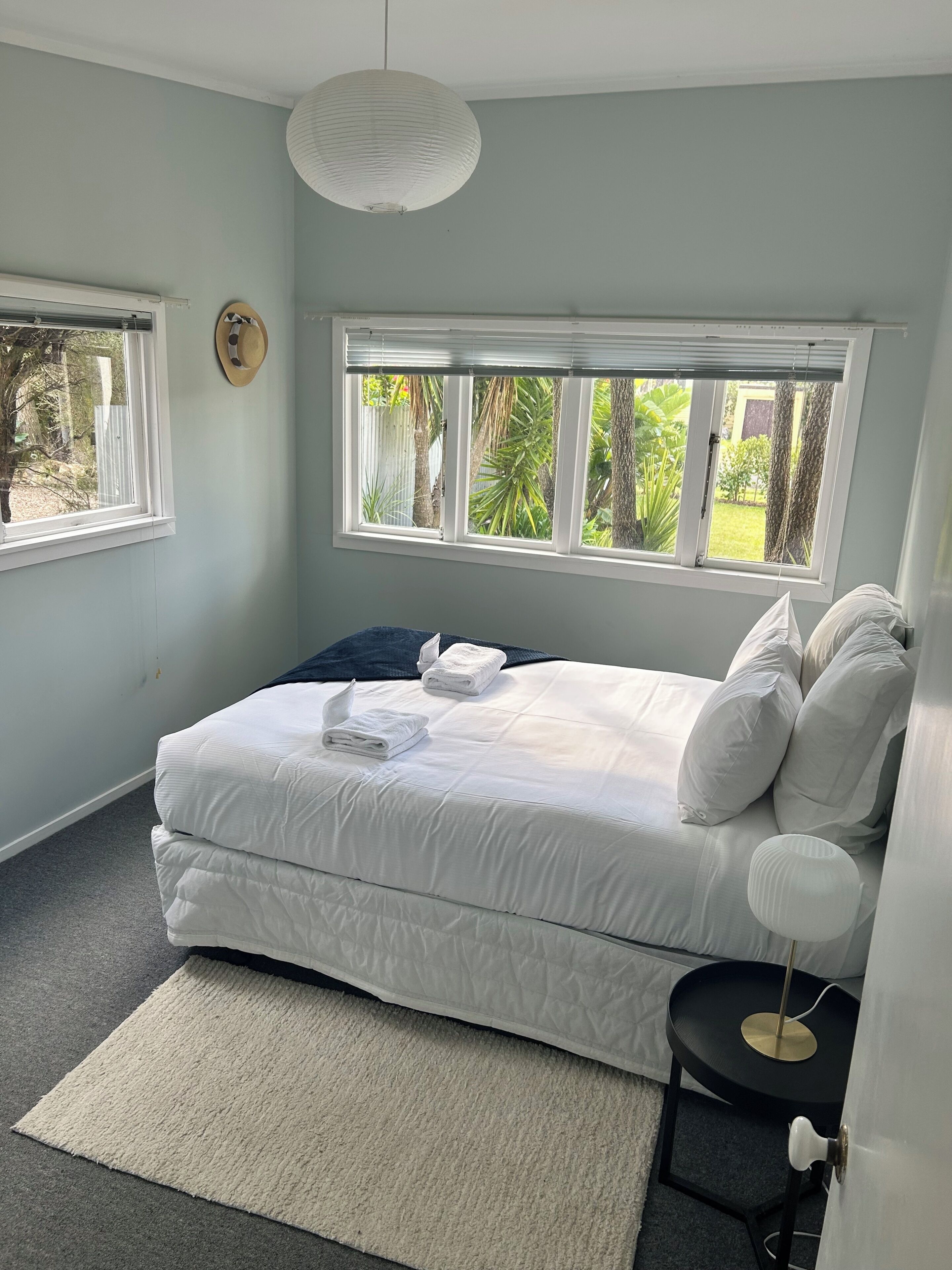 A bedroom with a bed, two windows, a bedside table, and a lamp.