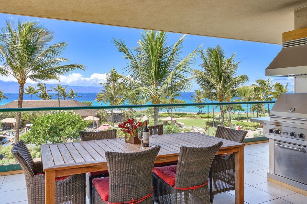 Ein Balkon mit Holztisch und Korbstühlen, mit Blick auf einen Strand mit Palmen und dem Meer.