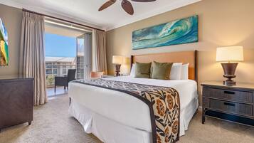 Quarto de hotel com cama, duas luminárias de cabeceira, ventoinha no teto, pintura e vista para o oceano.