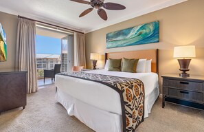 Ein Hotelzimmer mit einem Bett, zwei Nachttischlampen, einem Deckenventilator, einem Gemälde und Blick aufs Meer.
