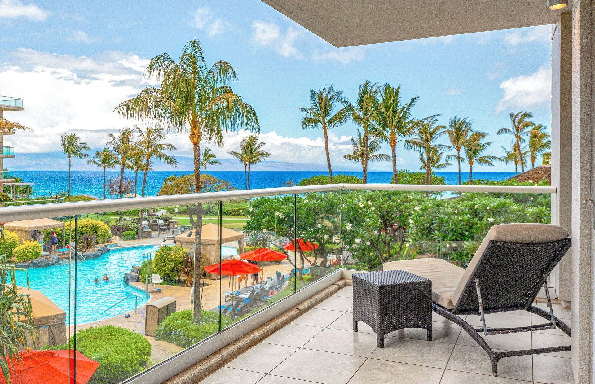 Un balcone con vista su una piscina e palme, che si affaccia sull'oceano.
