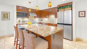 A modern kitchen with granite countertops, stainless steel appliances, and a central island with seating. - Honua Kai Resort & Spa by Maui Resort Rentals (Kaanapali)