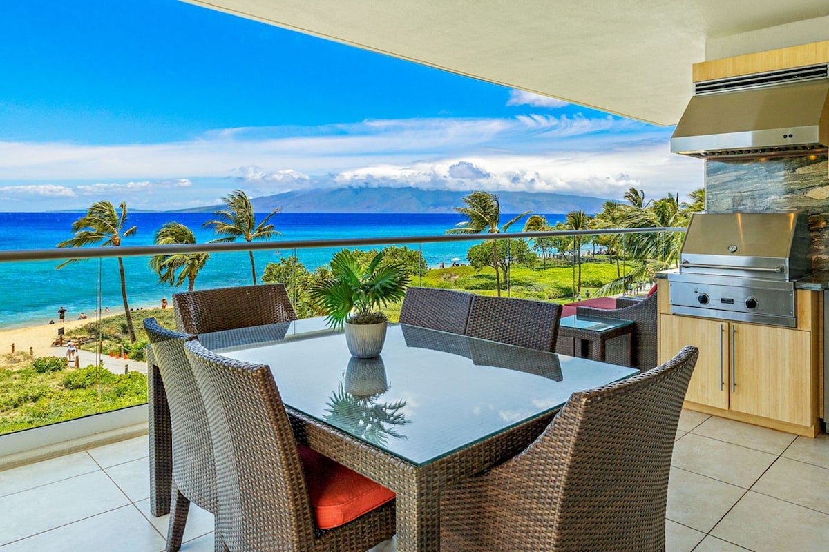 Ein Balkon mit Glastisch und Korbstühlen mit Blick auf Strand und Meer.