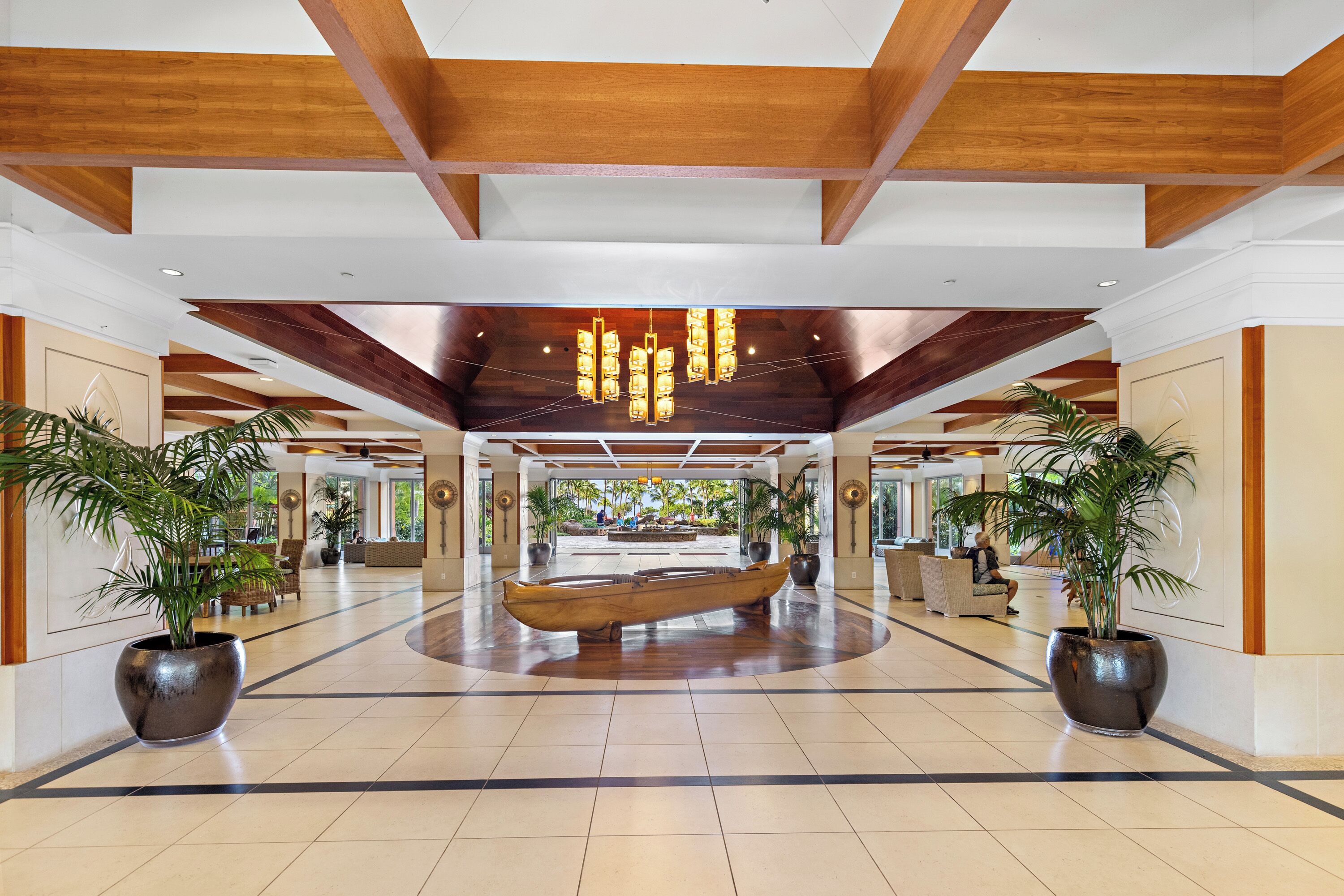 Um hall espaçoso com um barco de madeira como peça central, grandes vasos de plantas e um lustre moderno.