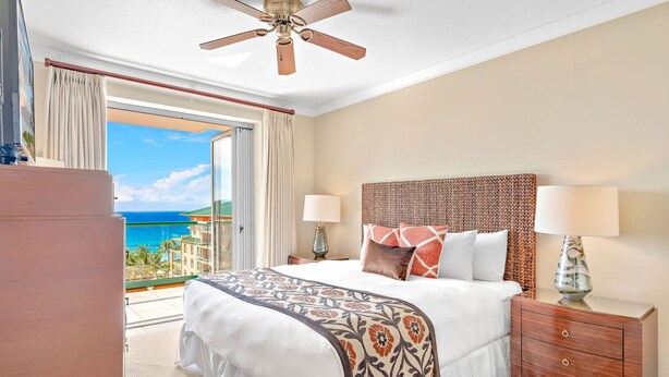 A hotel room with a bed, bedside tables, a ceiling fan, and a view of the ocean. - Honua Kai Resort & Spa by Maui Resort Rentals (Kaanapali)