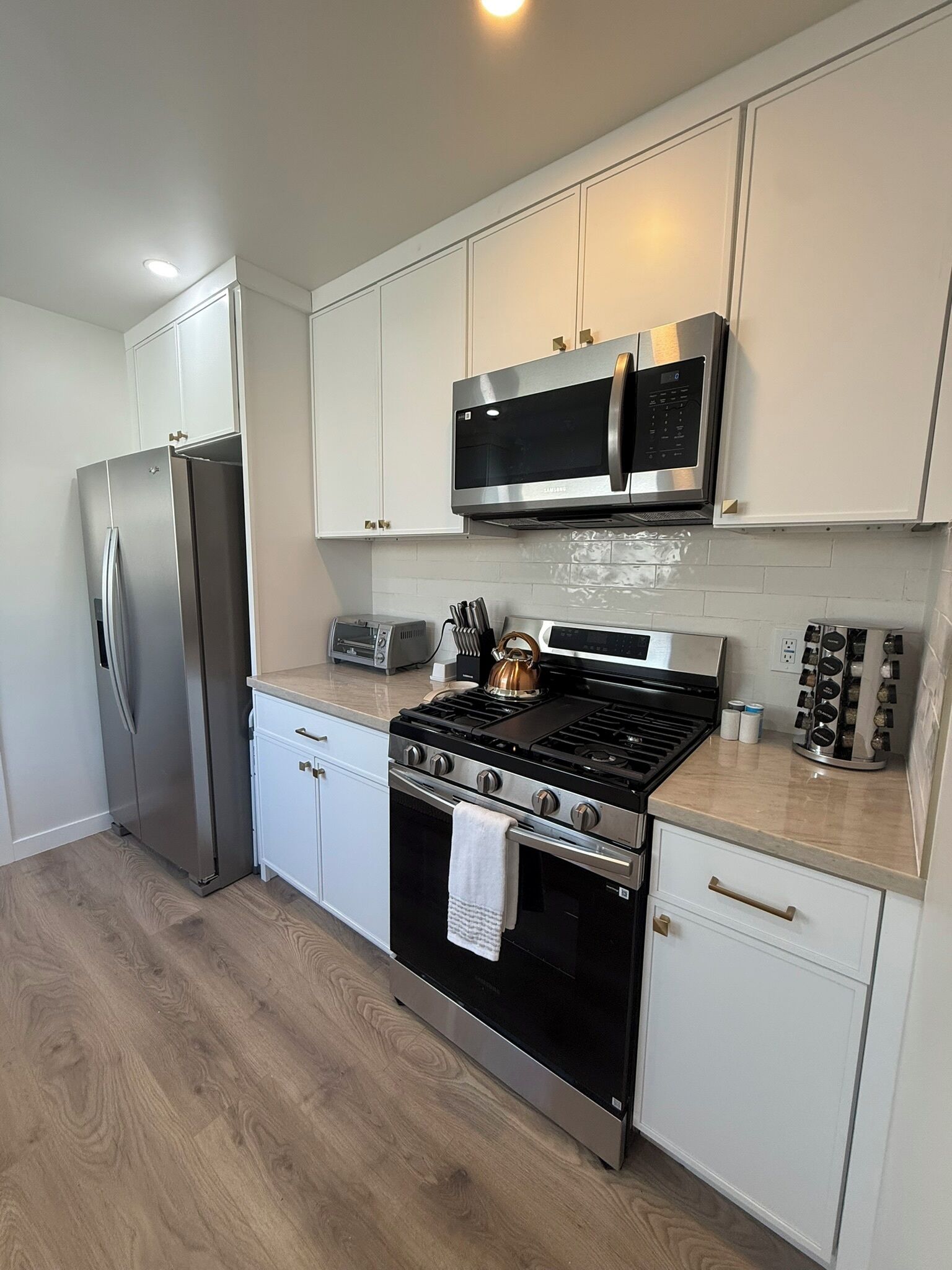 A modern kitchen with stainless steel appliances, white cabinetry, and a wood floor.