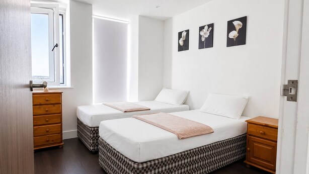 A bedroom with two beds, a window, a dresser, and wall art. - Modern 1BR Flat Sleeps 5 in Wimbledon (London)