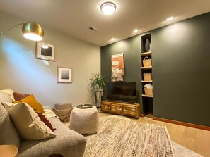 Ein Wohnzimmer mit Sofa, Hocker, Fernseher und Regalen mit Körben.