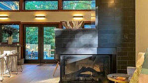 A modern living room with a fireplace, a dining area, and large windows. - The Retreat at Fox Lake (Athens Township)