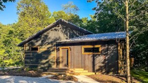 A wooden cabin with a gravel driveway, surrounded by trees. - The Retreat at Fox Lake (Athens Township)