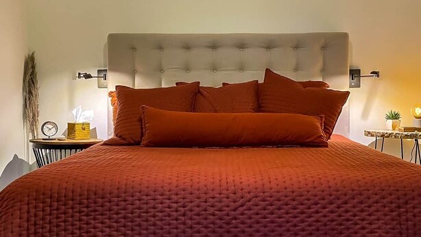 A bed with a tufted headboard, multiple pillows, and a bedside table with a lamp and a clock. - The Retreat at Fox Lake (Athens Township)