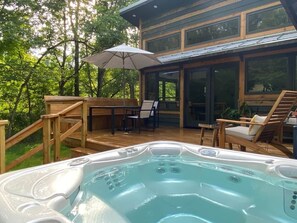 Un bain à remous sur une terrasse en bois, avec des meubles d’extérieur, et un bâtiment à l’arrière dont les parois sont en verre.