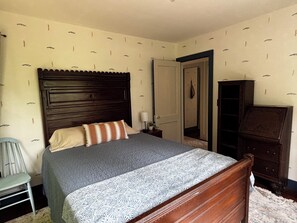 Ein Schlafzimmer mit einem hölzernen Bett, einem Nachttisch, einem Sessel und einem Kleiderschrank.