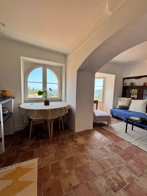 A cozy living area with a round table, a sofa, and a view through a window. - Au Levant, Charming Village House with Sea View (Bormes-les-Mimosas)