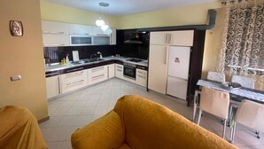 A compact kitchen with white cabinets, a dining table with chairs, and a patterned curtain. - Modern apartment (Shkodër)