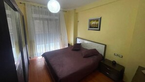 A bedroom with a bed, a nightstand, a wall-mounted picture, and a window with curtains. - Modern apartment (Shkodër)