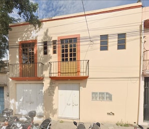 A building with two garage doors, a balcony with a metal railing, and a sign indicating medical services. - Mayor's House (Oaxaca de Juárez)