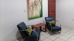 A room with two blue chairs, a small wooden table, and a painting of a tree on the wall. - Mayor's House (Oaxaca de Juárez)