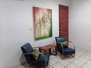 Ein Zimmer mit zwei blauen Stühlen, einem kleinen Holztisch und einem Baumgemälde an der Wand.