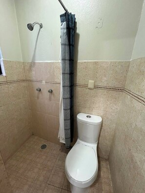 A small bathroom with a toilet, a shower curtain, and a wall-mounted faucet. - Mayor's House (Oaxaca de Juárez)