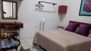 A bedroom with a bed, a bedside table, a mirror, a wall-mounted heater, a hanging light fixture, and a framed picture. - Mayor's House (Oaxaca de Juárez)