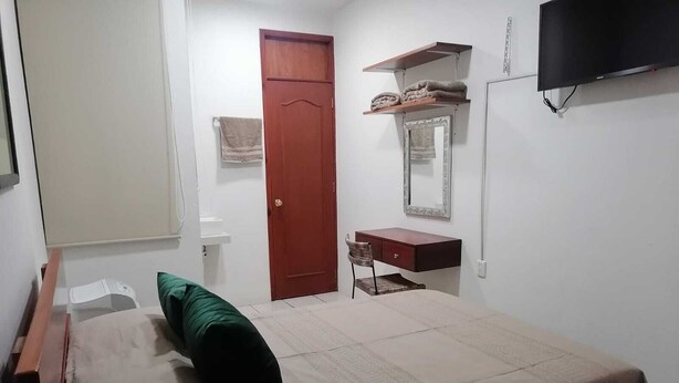 A bedroom with a bed, a desk, a chair, a wardrobe, a mirror, and a television. - Mayor's House (Oaxaca de Juárez)