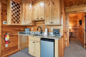 A wooden cabin interior with a kitchen area featuring a granite countertop, a dishwasher, and wooden cabinets. - High Smokies Lodge: Game Room, Hot Tub, Pet-Friendly (Sevierville)