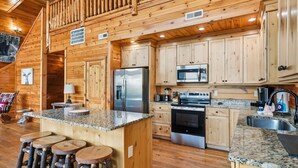 A log cabin interior with a kitchen featuring granite countertops, stainless steel appliances, and wooden cabinetry. - High Smokies Lodge - Game Room, Hot Tub and more! (Sevierville)