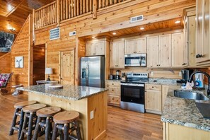 A log cabin interior with a kitchen featuring granite countertops, stainless steel appliances, and wooden cabinetry. - High Smokies Lodge - Game Room, Hot Tub and more! (Sevierville)