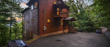A log cabin with a staircase leading to a porch, surrounded by trees.