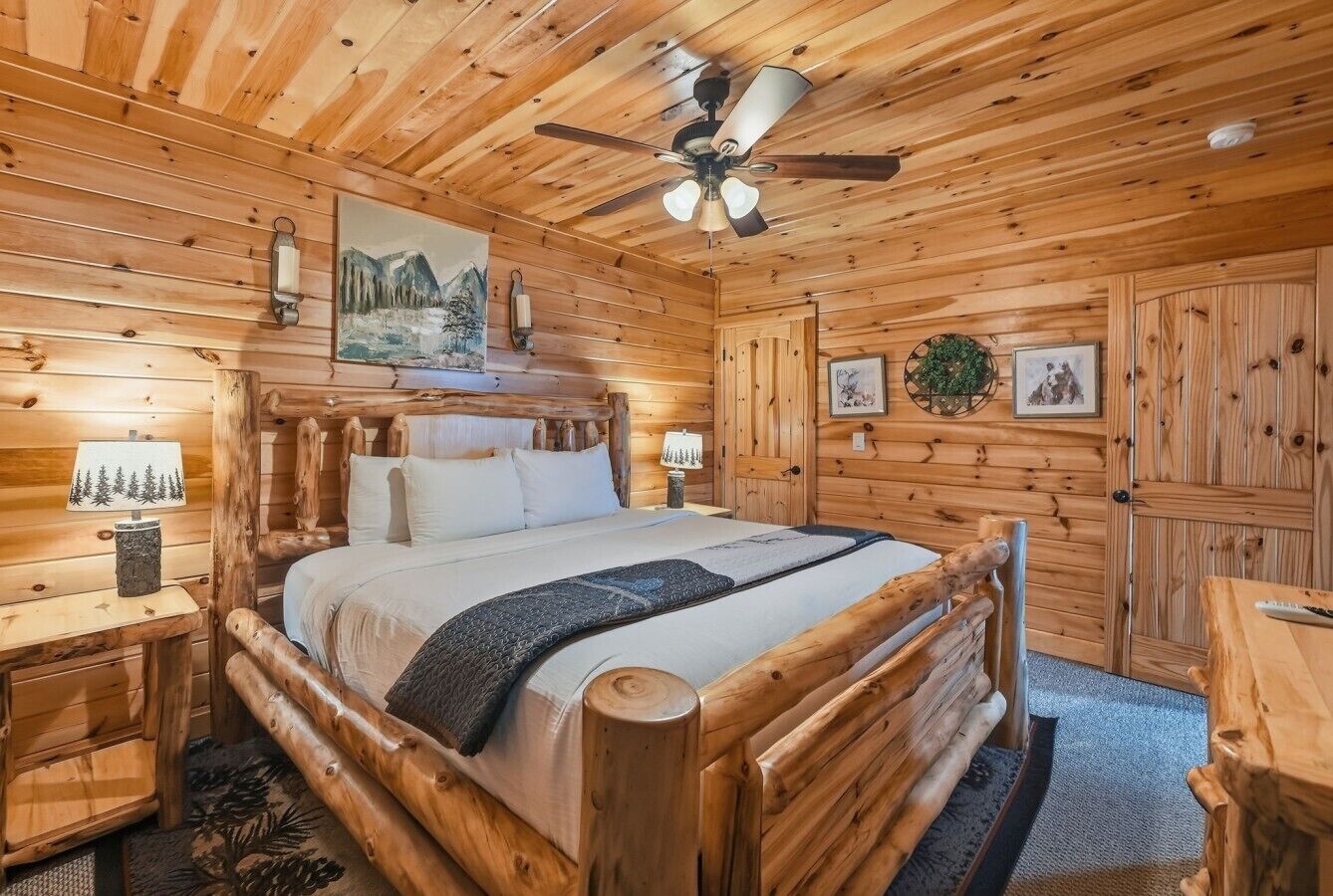 A wooden cabin interior with a bed, a ceiling fan, and a fireplace.