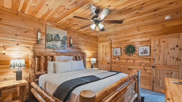 A wooden cabin interior with a bed, a ceiling fan, and a fireplace. - High Smokies Lodge - Game Room, Hot Tub and more! (Sevierville)