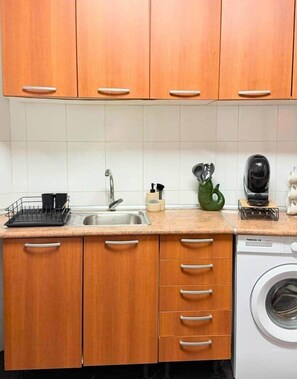 A kitchen with wooden cabinets, a sink, a dish rack, a coffee maker, and a washing machine. - Church View by Stayguest (Santa Cruz)