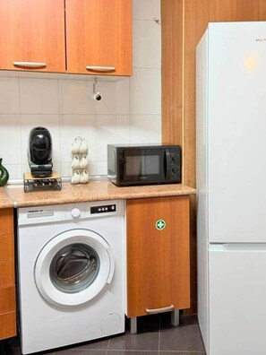 Eine kleine Küche mit Waschmaschine, Mikrowelle und Kühlschrank.