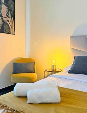 Een hotelkamer met een bed, een bedlampje, een stoel en een schilderij aan de muur.