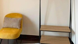 Una stanza con una sedia gialla, un quadro incorniciato e un appendiabiti nero in metallo con grucce in legno.