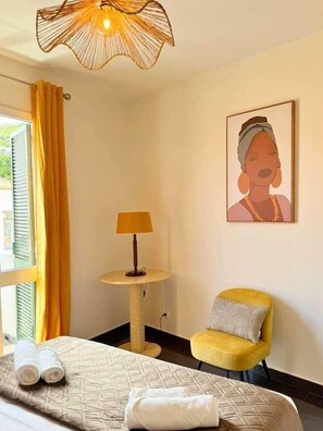 Ein Hotelzimmer mit Bett, Sessel, Lampe, einem Gemälde und einem Fenster mit Vorhängen.