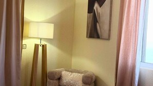Et hotelværelse med en seng, en stol, et lille bord, en lampe og et maleri på væggen.