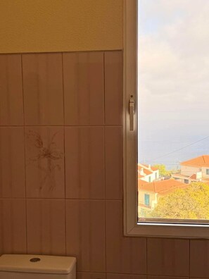 A bathroom with a toilet, a window, and a view of buildings outside. - Recanto da Bemposta by Stayguest (Machico)