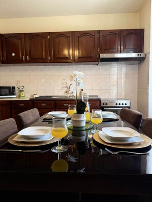 A kitchen with dark wooden cabinets, a stainless steel range hood, and a dining table set with plates, glasses, and a vase with flowers. - Recanto da Bemposta by Stayguest (Machico)