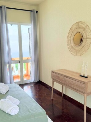 A hotel room with a bed, a wooden bedside table, a wall-mounted mirror, and a view through a glass door. - Recanto da Bemposta by Stayguest (Machico)